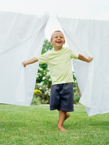 Boy standing between sheets hanging on a clothesline